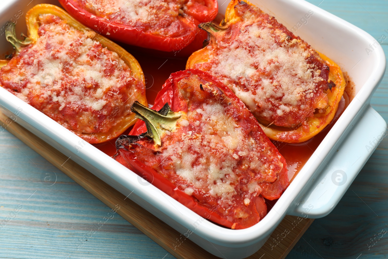 Photo of Tasty stuffed peppers in dish on light blue wooden table, closeup