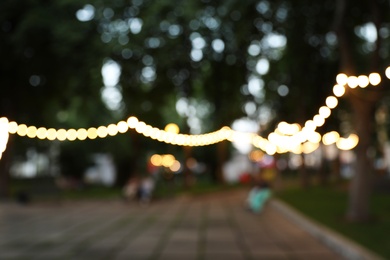 Blurred view of street with garland in evening. Bokeh effect