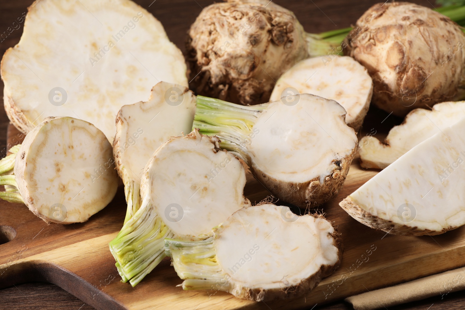 Photo of Whole and cut celery roots on wooden table, closeup