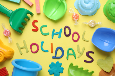 Photo of Flat lay composition with phrase School Holidays made of modeling clay on yellow background