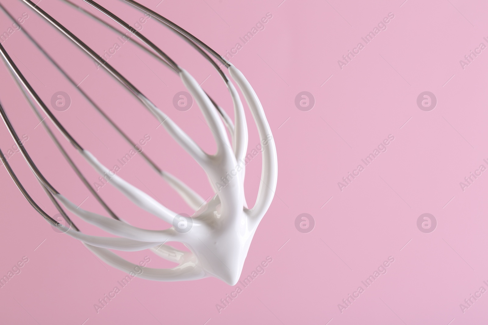 Photo of Whisk with whipped cream on pink background, closeup. Space for text