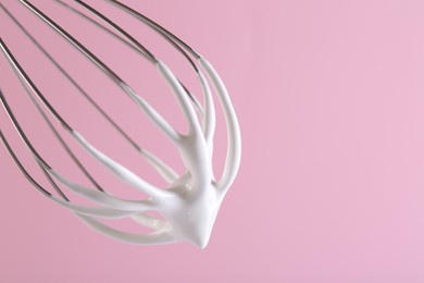 Whisk with whipped cream on pink background, closeup. Space for text