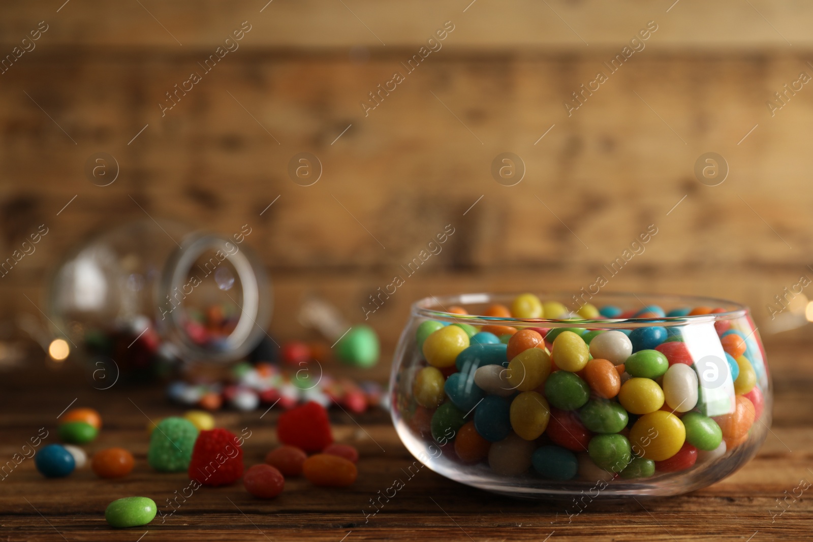 Photo of Delicious dragee in bowl on wooden table, closeup. Space for text