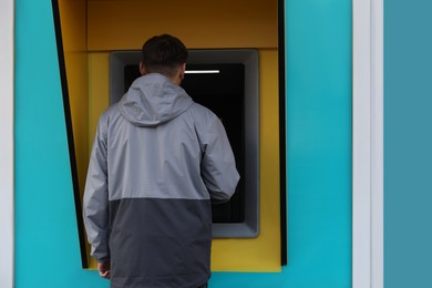 Photo of Man using modern cash machine outdoors, back view