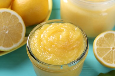Photo of Delicious lemon curd in glass jar and fresh citrus fruits on light blue table, closeup