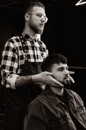 Image of Professional hairdresser working with bearded client in barbershop. Black and white effect