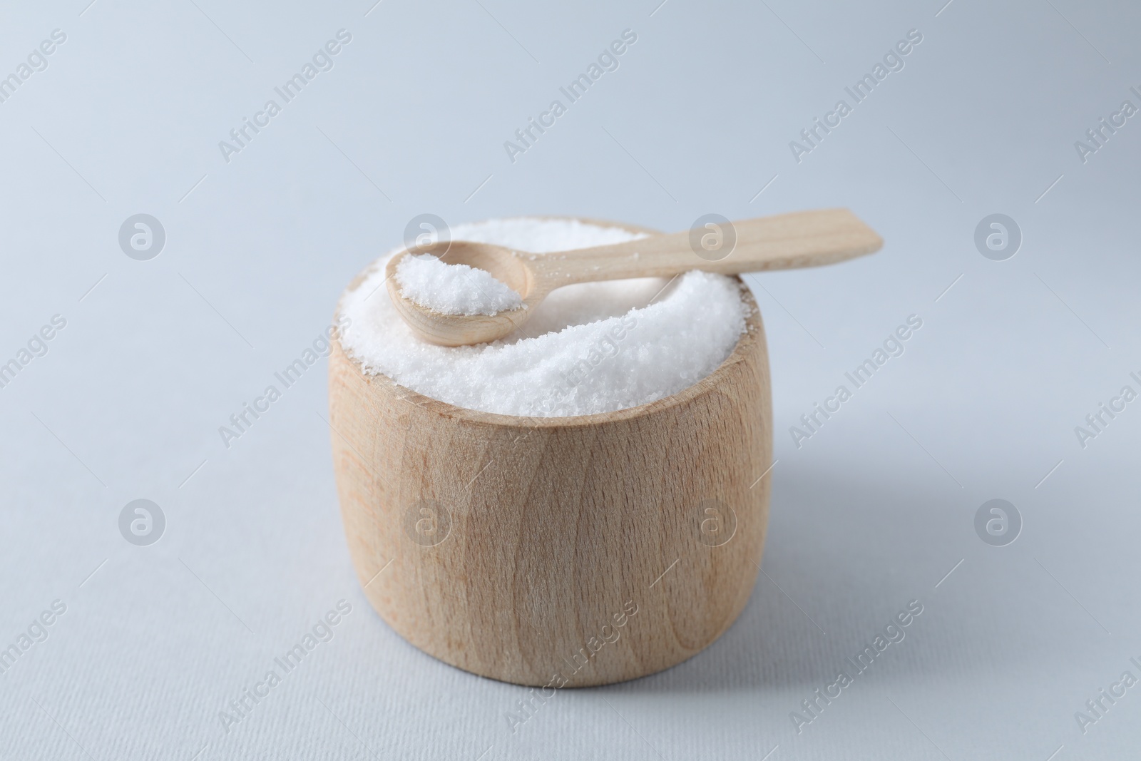 Photo of Organic white salt in bowl and spoon on light grey background, closeup