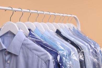 Dry-cleaning service. Many different clothes in plastic bags hanging on rack against beige background, closeup