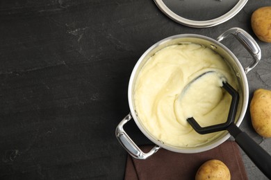 Pot of freshly cooked homemade mashed potatoes and raw vegetables on black table, flat lay. Space for text