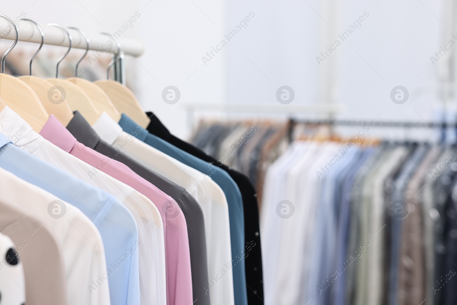 Photo of Dry-cleaning service. Many different clothes hanging on rack indoors, closeup