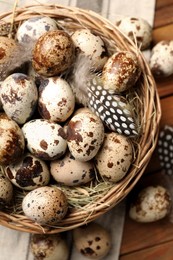 Photo of Speckled quail eggs and feathers on wooden table, flat lay