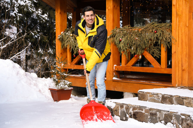 Man removing snow from house yard with shovel on winter day