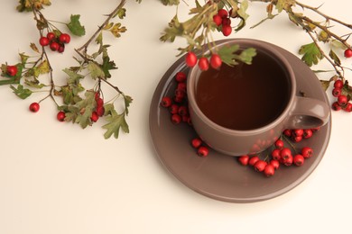 Aromatic hawthorn tea in cup and branch with berries on beige table, above view. Space for text