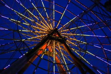 Photo of Beautiful glowing Ferris wheel against dark sky, low angle view