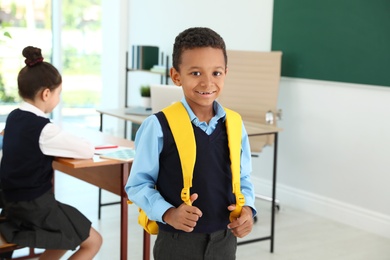 African-American boy wearing school uniform with backpack in classroom