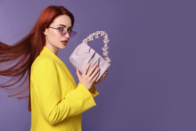 Photo of Stylish woman with red dyed hair and bag on purple background, space for text
