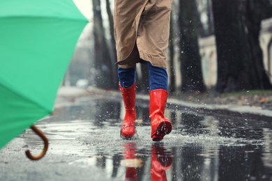Photo of Woman in rubber boots running after umbrella outdoors on rainy day, closeup