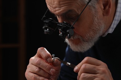 Photo of Professional jeweler working with ring on dark background, closeup