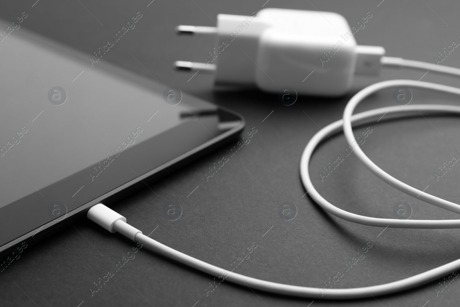 Photo of Tablet and charger on black background, closeup. Modern technology