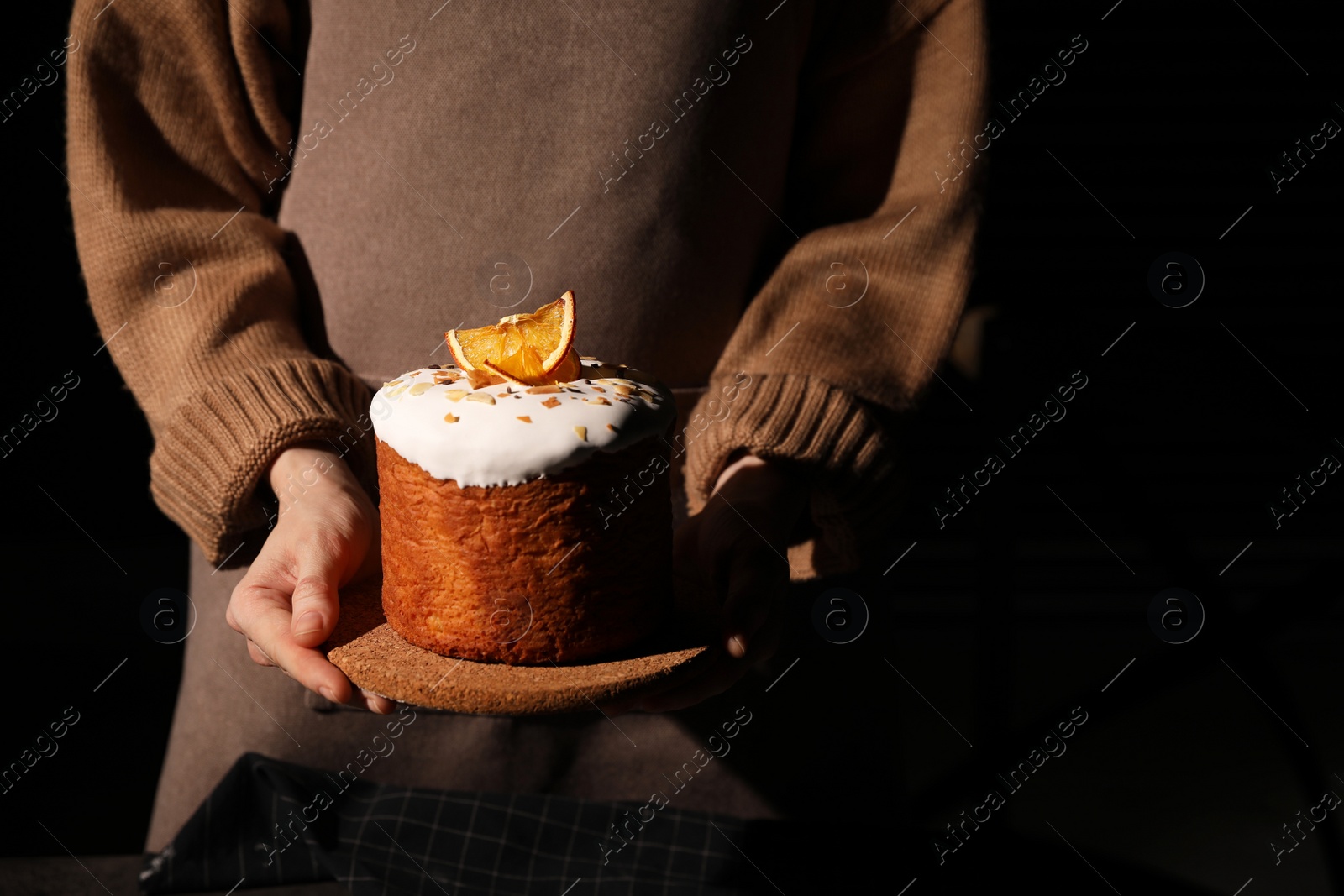 Photo of Young woman holding traditional decorated Easter cake on black background, closeup