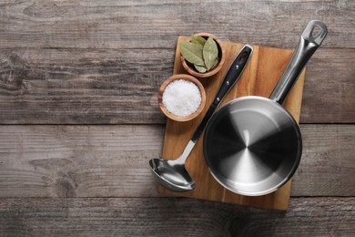 Photo of Steel saucepan, board, ladle and spices on wooden table, top view. Space for text