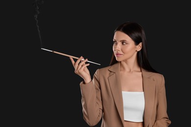 Woman using long cigarette holder for smoking on black background