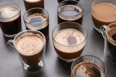 Many cups of different aromatic hot coffee on grey background