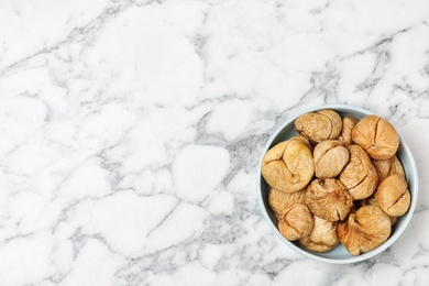 Bowl of dried figs on marble table, top view with space for text. Healthy fruit