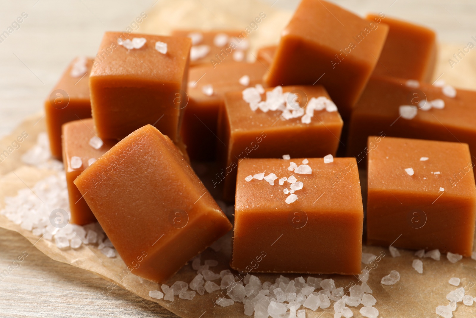 Photo of Tasty caramel candies and sea salt on light wooden table, closeup