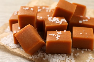 Photo of Tasty caramel candies and sea salt on light wooden table, closeup