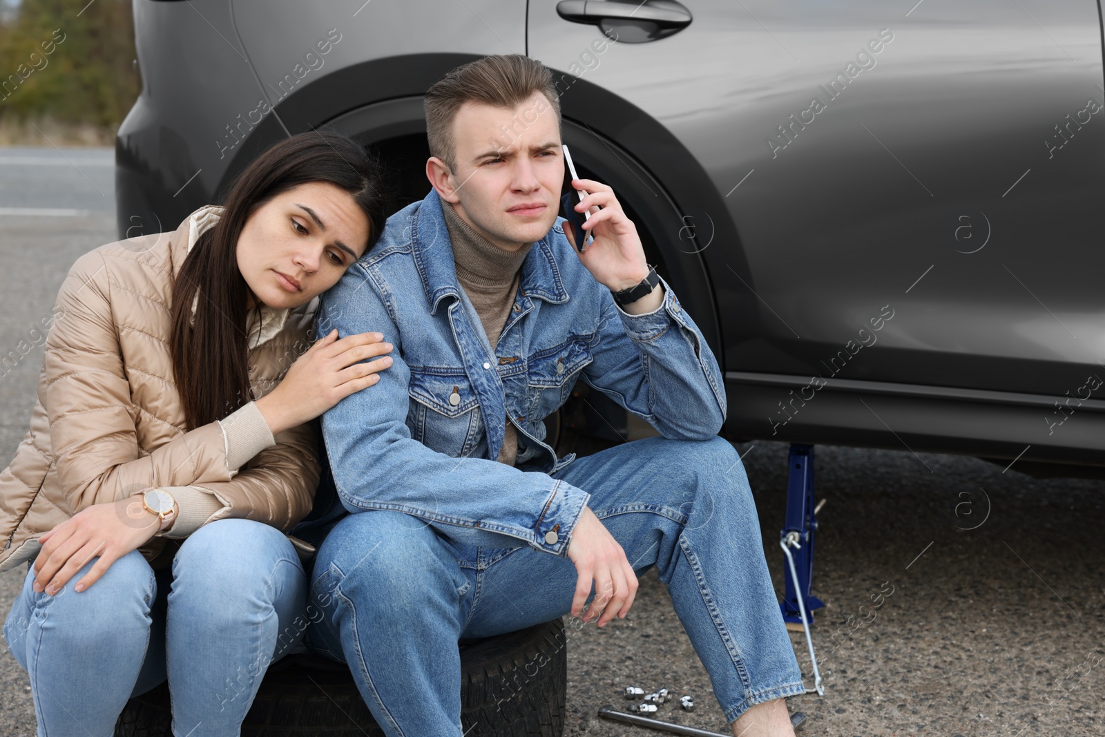 Photo of Young man calling to car service on roadside. Tire puncture