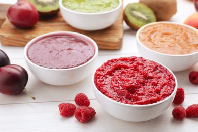 Different puree in bowls and fresh fruits on white wooden table