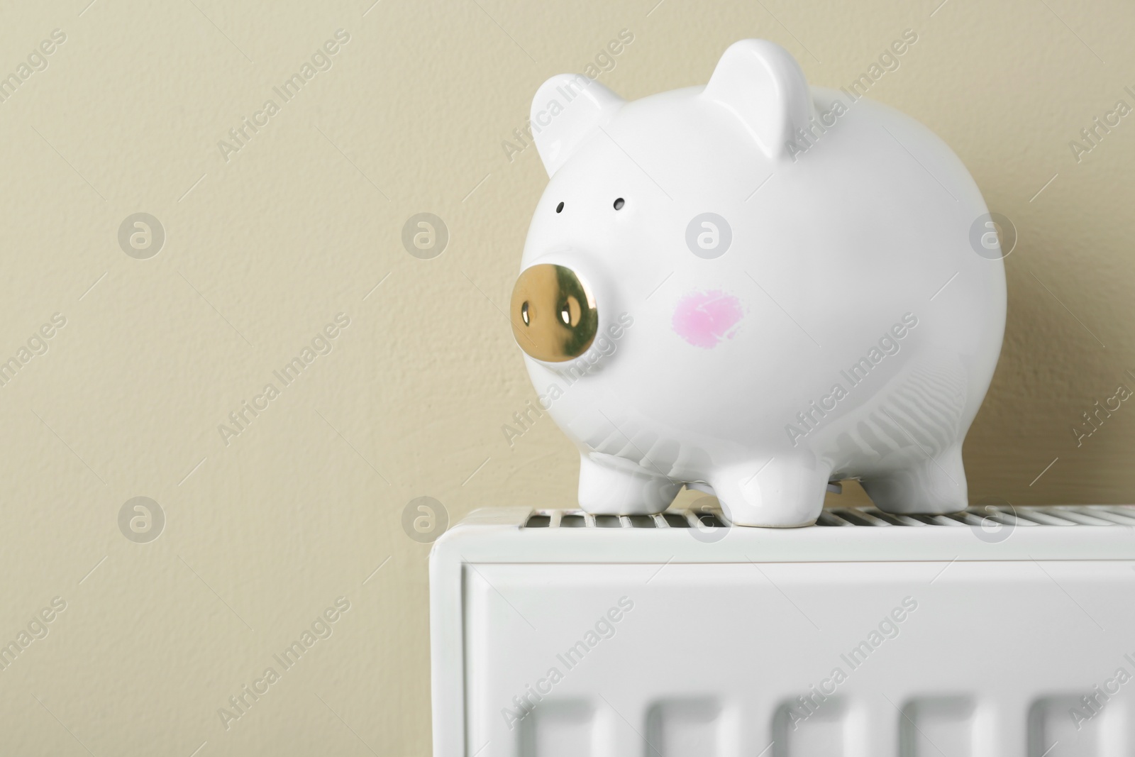 Photo of Piggy bank on heating radiator against beige background, space for text