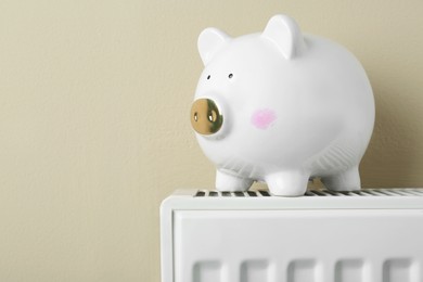 Piggy bank on heating radiator against beige background, space for text