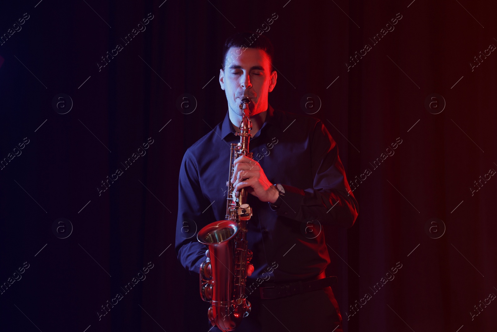 Photo of Young man playing saxophone on dark background