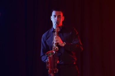 Photo of Young man playing saxophone on dark background