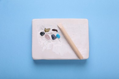 Photo of Educational toy for motor skills development. Excavation kit (plaster, wooden chisel and gemstones) on light blue background, top view