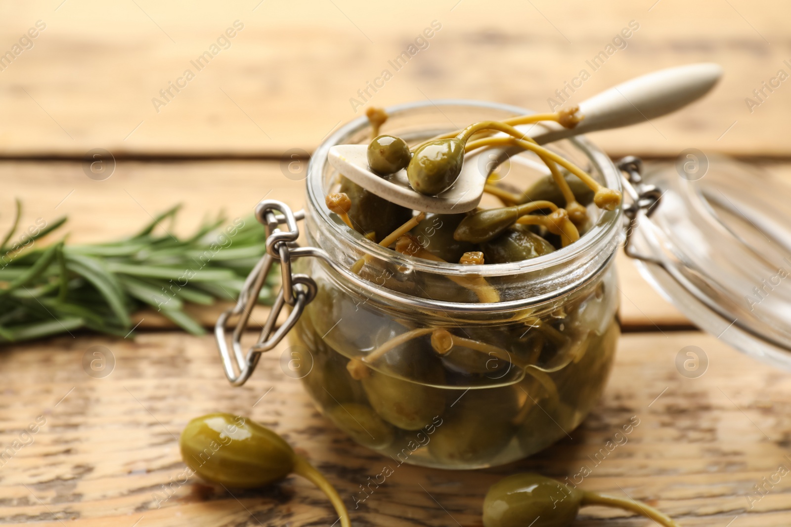 Photo of Delicious pickled capers in glass jar on wooden table, closeup