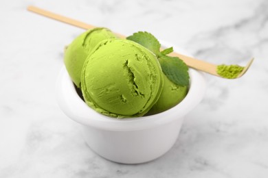 Photo of Tasty matcha ice cream in bowl and spoon with powder on white marble table
