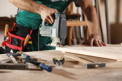 Photo of Professional carpenter working with jigsaw at workbench, closeup