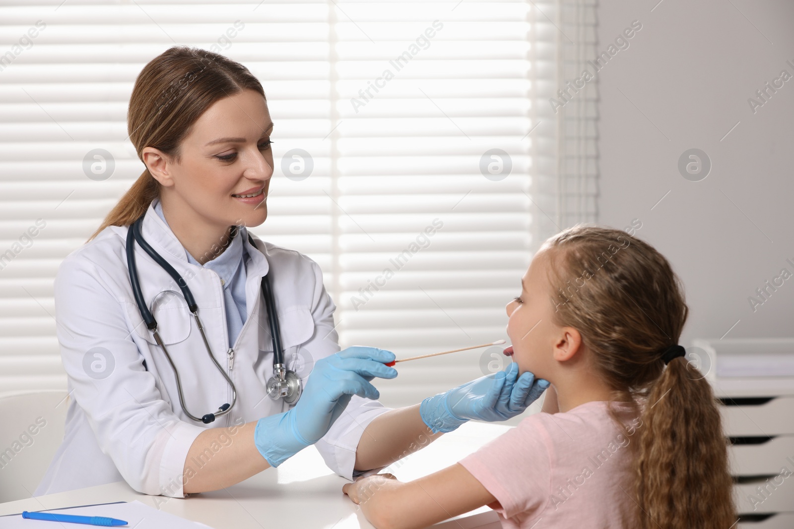 Photo of Doctor taking throat swab sample from girl`s oral cavity indoors