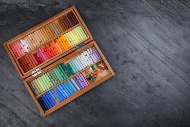 Photo of Set of colorful pastels in wooden box on grey stone table, top view with space for text. Drawing materials