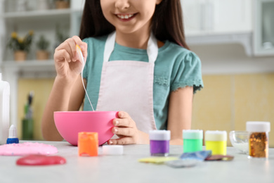 Photo of Little girl mixing ingredients with silicone spatula at table in kitchen, closeup. DIY slime toy