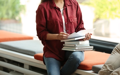 Photo of Young woman with books sitting near window in library, closeup