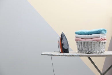 Photo of New modern iron and basket with laundry on board against color background, space for text