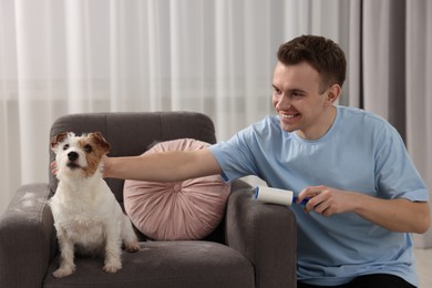 Photo of Smiling man removing pet's hair from armchair at home