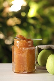 Photo of Glass jar with delicious apple jam and fresh fruits on white wooden table against blurred background, closeup. Space for text