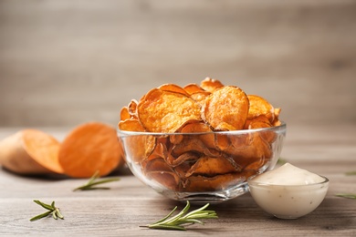 Photo of Delicious sweet potato chips in bowl, rosemary and sauce on table