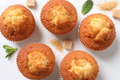 Delicious sweet muffins and brown sugar on white table, flat lay