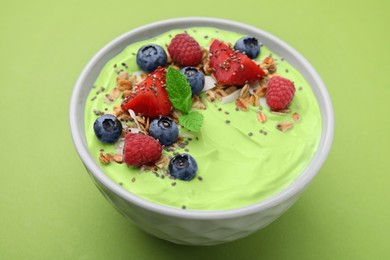 Tasty matcha smoothie bowl served with berries and oatmeal on green background. Healthy breakfast